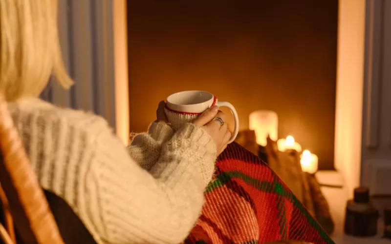 Partial view of woman in checkered blanket holding mug of cocoa at home